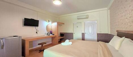 Habitación de hotel con cama, televisión, minibar, escritorio y silla, y una puerta.