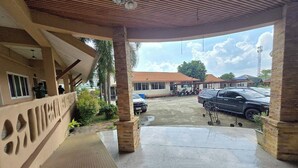 Un espace extérieur abrité, doté d’un sol en béton, d’un plafond en bois et offrant une vue sur les voitures garées et les bâtiments situés au loin.