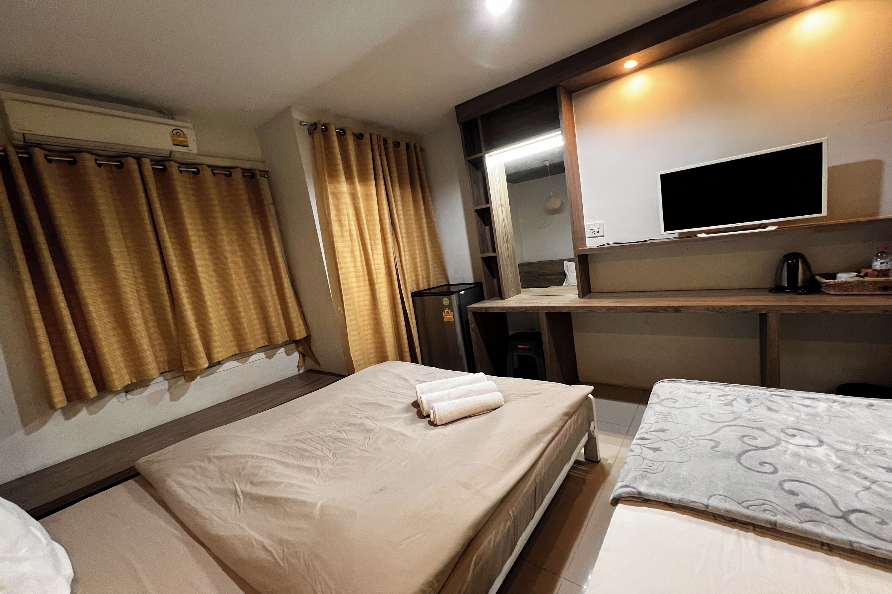 Ein Hotelzimmer mit zwei Betten, einem Fernseher, einem Schreibtisch und einem Spiegel.