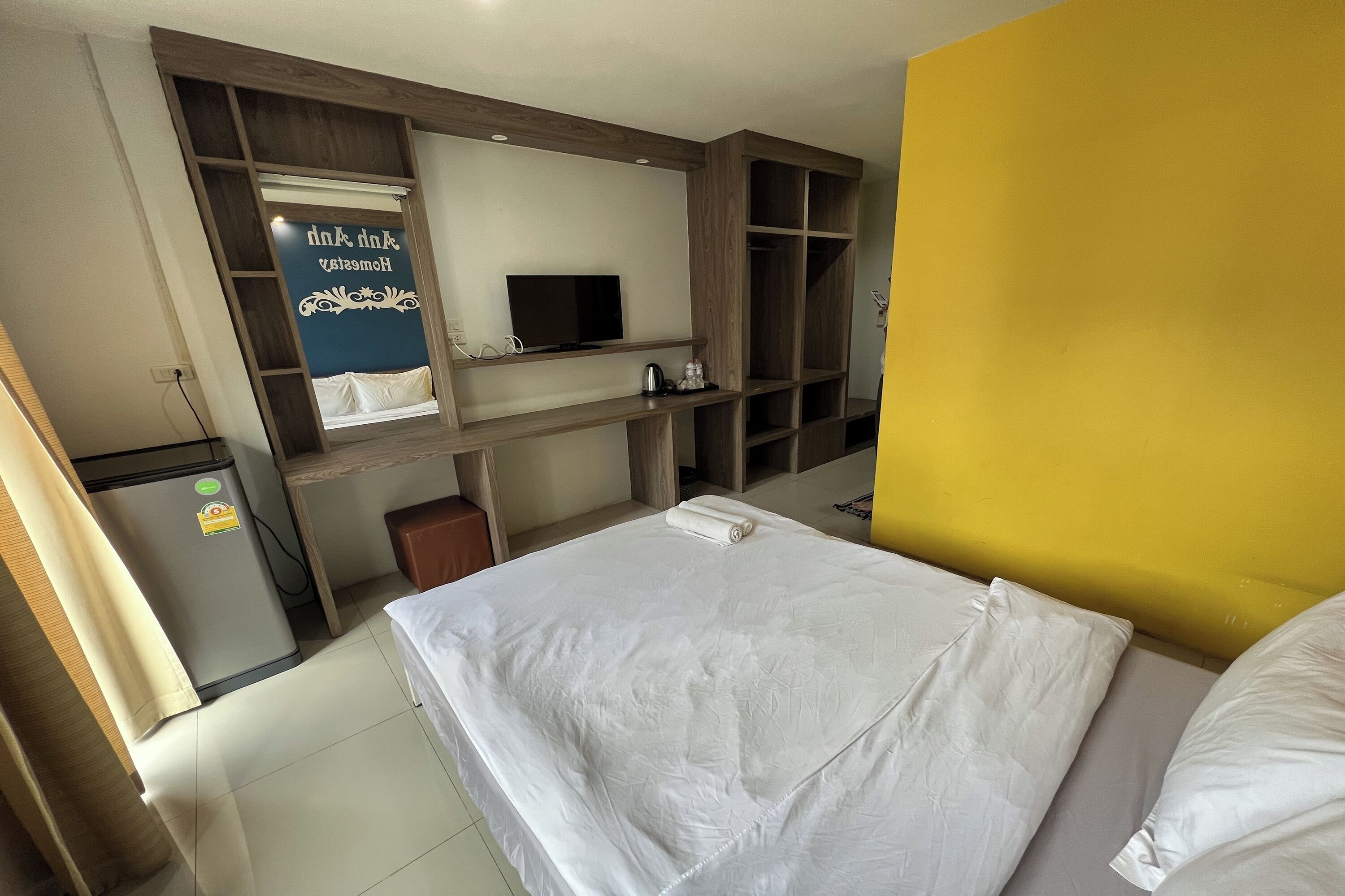 A hotel room with a bed, a desk with a computer, a TV, and a minibar.