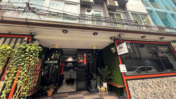 Entrada de hotel com porta de vidro, plantas em vasos e um letreiro com 'Homestay'.