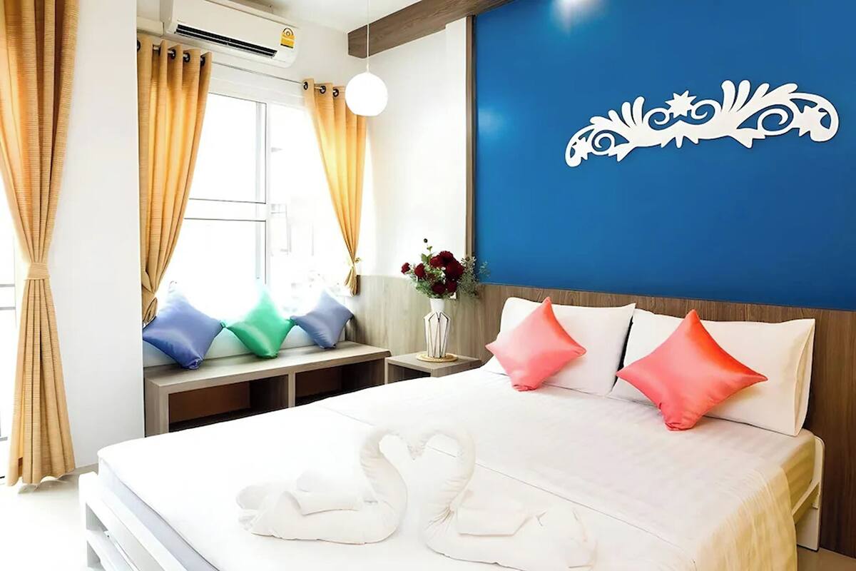 A hotel room with a bed, pillows, a vase with flowers, and a decorative wall piece.