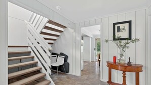 Uma escadaria com grades brancas e degraus castanhos que levam a um quarto com uma mesa e cadeiras de madeira.