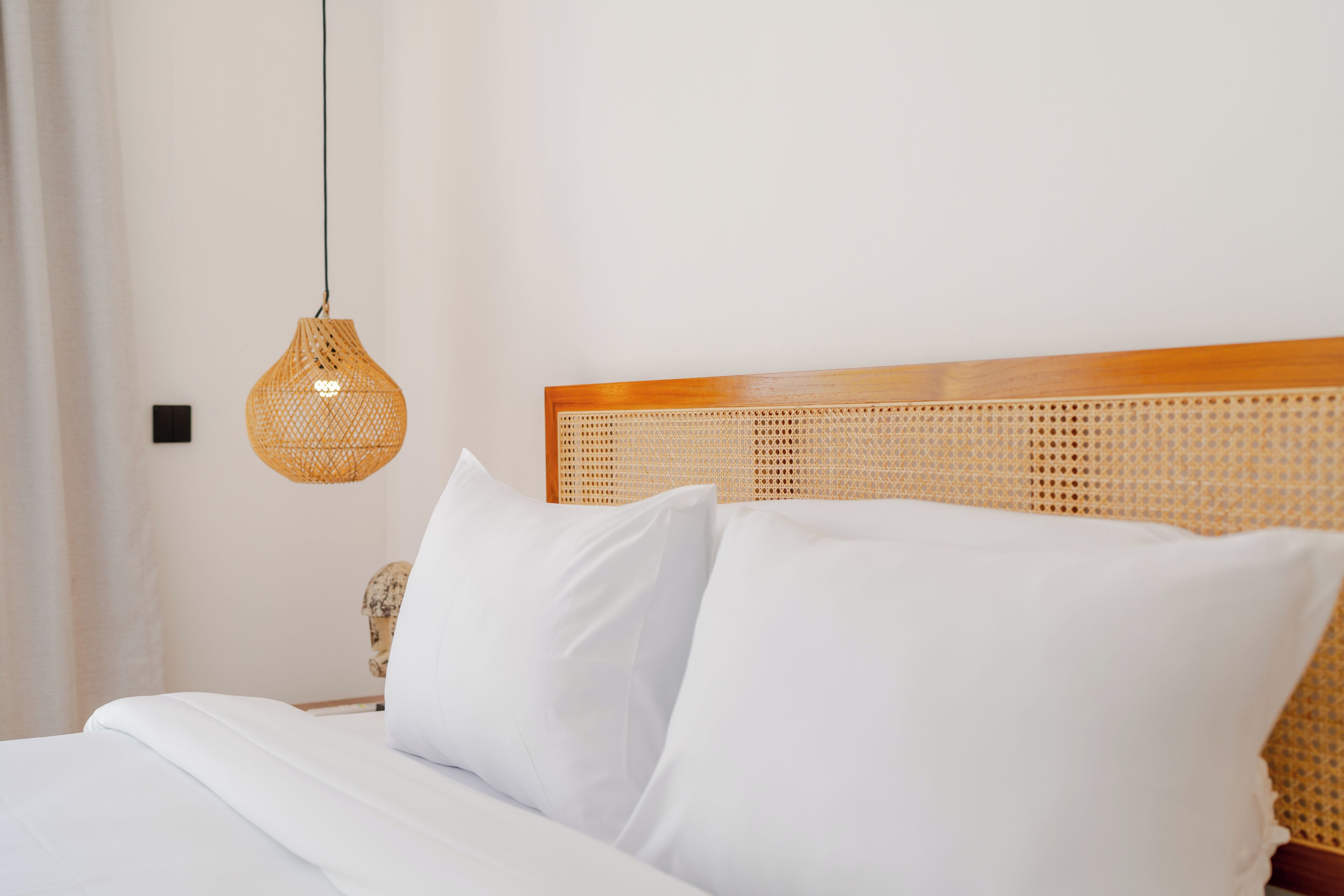 A neatly made bed with white linens and a woven headboard.