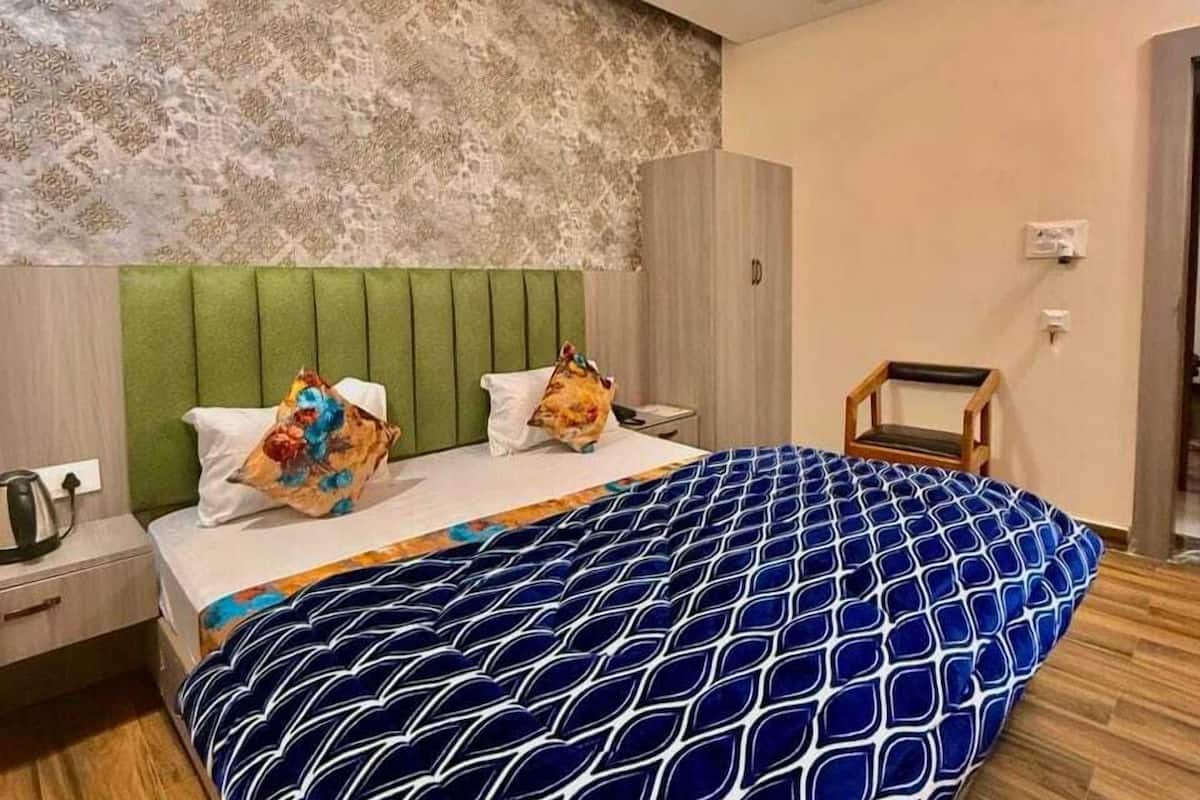 A modern bedroom with a patterned bedspread, a green headboard, a ceiling fan, and a wooden floor.