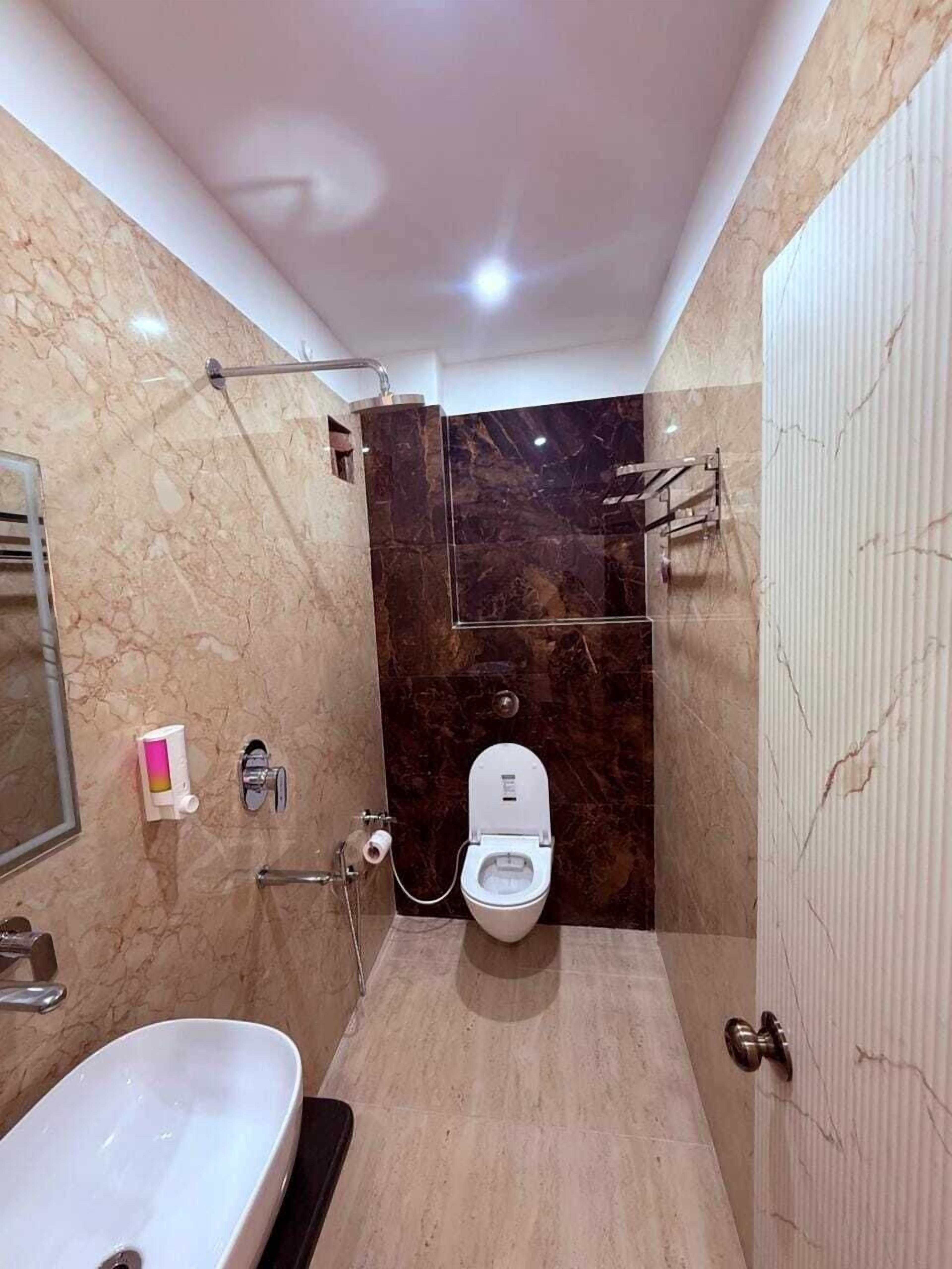 Un baño con pared de mármol, inodoro blanco, lavamanos y zona de ducha.