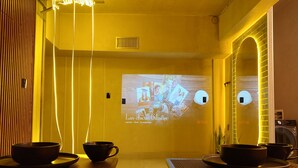 A room with a projection screen displaying 'Las chicas Gilmore' on the wall, two tables with bowls and spoons, and a brick-patterned wall.