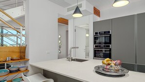 Eine moderne Küche mit einer zentralen Kochinsel, weißen Barhocker, einem eingebauten Backofen und einer hängenden Leuchte.