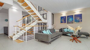 Ein modernes Wohnzimmer mit einer Holztreppe, grauen Sofas und abstrakter Wandkunst.