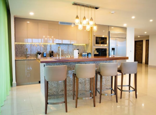 Una cocina moderna con encimera de granito, electrodomésticos de acero inoxidable y una zona de bar con cuatro taburetes.