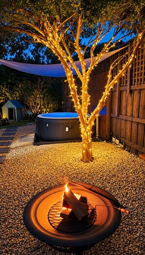 Un patio trasero con un jacuzzi, un árbol iluminado con luces y un pozo de fuego.