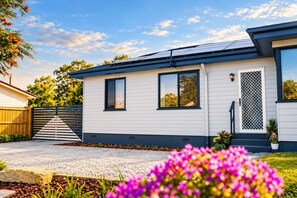 A modern single-story house with a solar panel roof, a front door with a security screen, and a driveway leading to a gated entrance.