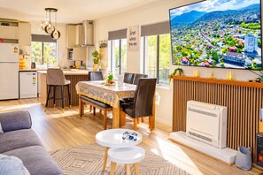 A modern kitchen with a dining area, a flat-screen TV displaying a cityscape, and a living room with a sofa and coffee table.