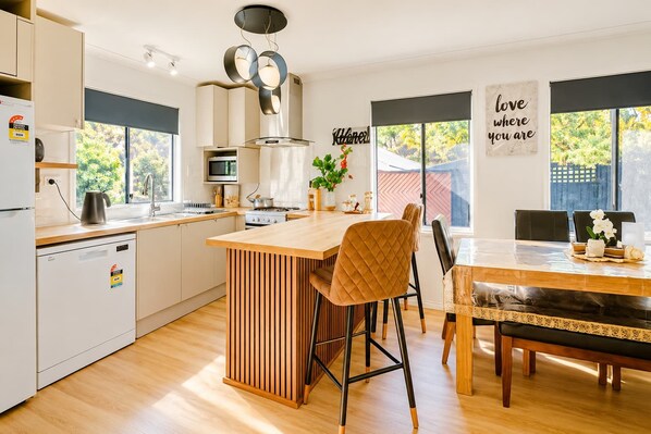 A modern kitchen with a central island, a dining area with a bench, and a view of the outdoors.