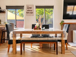 Un comedor con mesa de madera, sillas con acolchado negro y un banco. Hay un letrero en la pared que dice 'love where you are'.