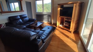 A living room with a black leather sofa, a wooden coffee table, and a TV stand with shelves. - Apartment with private terrace, in the country and in the city at the same time. (Privas)