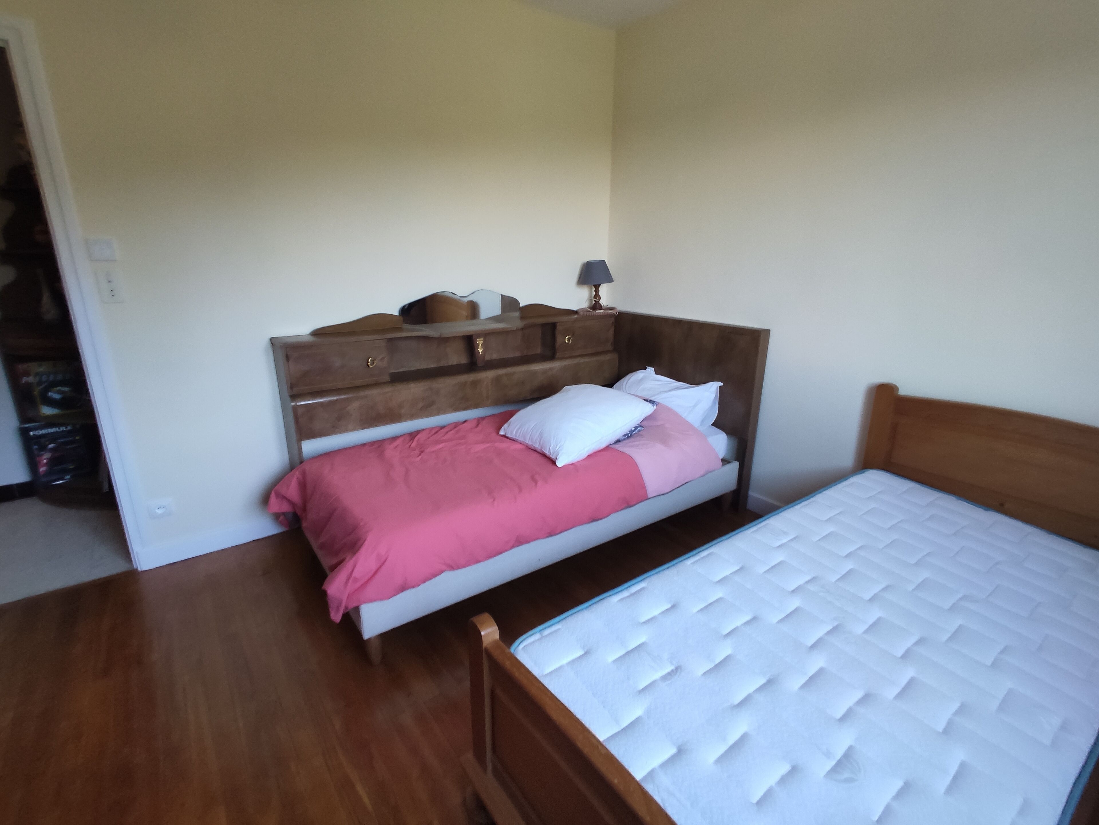 A bedroom with a wooden bed frame, a white mattress, and a pink bedspread.