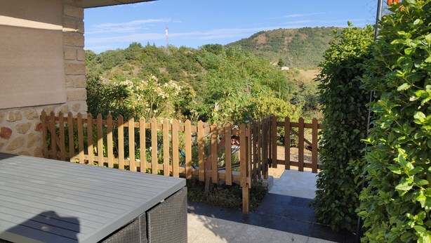 A patio area with a stone wall, a wooden fence, and a view of a hillside. - Apartment with private terrace, in the country and in the city at the same time. (Privas)