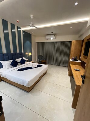 Una habitación de hotel moderna con una cama grande, un escritorio, una silla, un ventilador de techo, un equipo de aire acondicionado y un televisor.