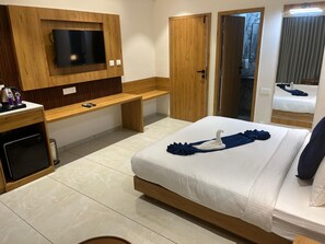 Ein Hotelzimmer mit einem Bett, einem an einer Holzplatte montierten Fernseher, einer Bank, einem Schreibtisch mit Wasserkocher und einem Mülleimer.