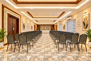 Un salón de conferencias con filas de sillas, una mesa larga y paneles decorativos en las paredes.