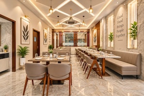 A restaurant with a long dining table, multiple seating options, and a modern interior design. - Hotel Premji by Shivalaya Darshanam (Dwarka)