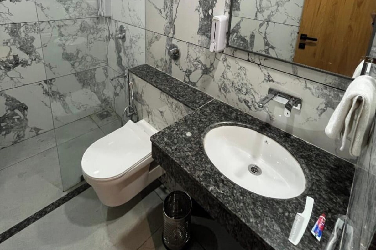 Un baño moderno con paredes de mármol, cabina de ducha de vidrio, inodoro y lavamanos con espejo.