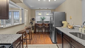 A modern kitchen with granite countertops, a stainless steel refrigerator, and a dining area with wooden chairs and a table. - Cozy 1BR Retreat in Central West End with Fireplace, Sofa Bed & City Views (St. Louis)
