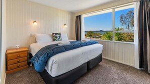 Een slaapkamer met een groot bed, een nachtkastje, een raam met uitzicht op de omgeving en een plafondlamp.