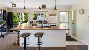 Een moderne keuken met een centraal eiland, hangende verlichting en uitzicht op het groen.