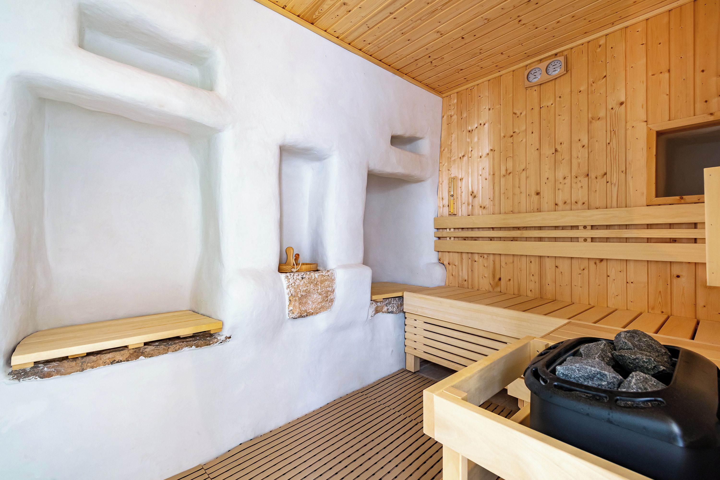 Un sauna con bancos de madera, una pileta de piedra y una pared de madera con un reloj.