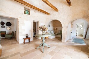 A rustic interior with stone walls, a round table with a vase, and a sofa. - Masseria Maranna Trulli&spa Luxury Villa (Martina Franca)