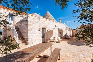 A stone building with a tiled roof, a wooden bench, and a table with chairs in an outdoor setting. - Masseria Maranna Trulli&spa Luxury Villa (Martina Franca)