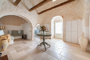 A rustic interior with exposed stone walls, a round table with a vase, and a large white vase. - Masseria Maranna Trulli&spa Luxury Villa (Martina Franca)