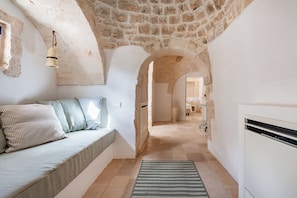 A narrow hallway with a stone ceiling, a sofa with striped pillows, and a patterned rug. - Masseria Maranna Trulli&spa Luxury Villa (Martina Franca)