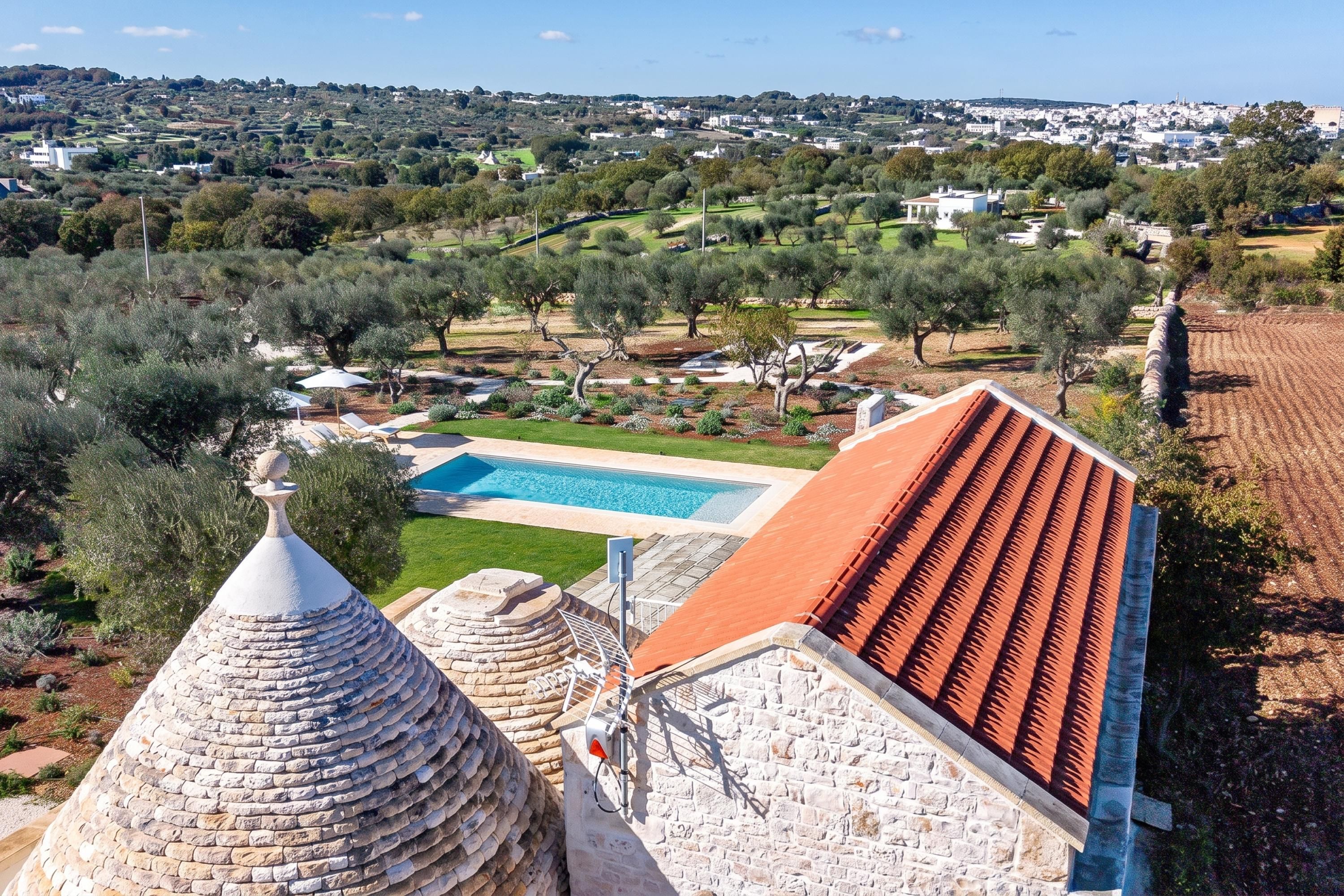 A villa with a swimming pool, stone architecture, and a view of a town.