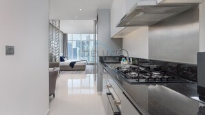 Une cuisine moderne dotée d’une hotte en acier inoxydable, d’un plan de travail noir et offrant une vue sur la ville grâce à de grandes fenêtres.