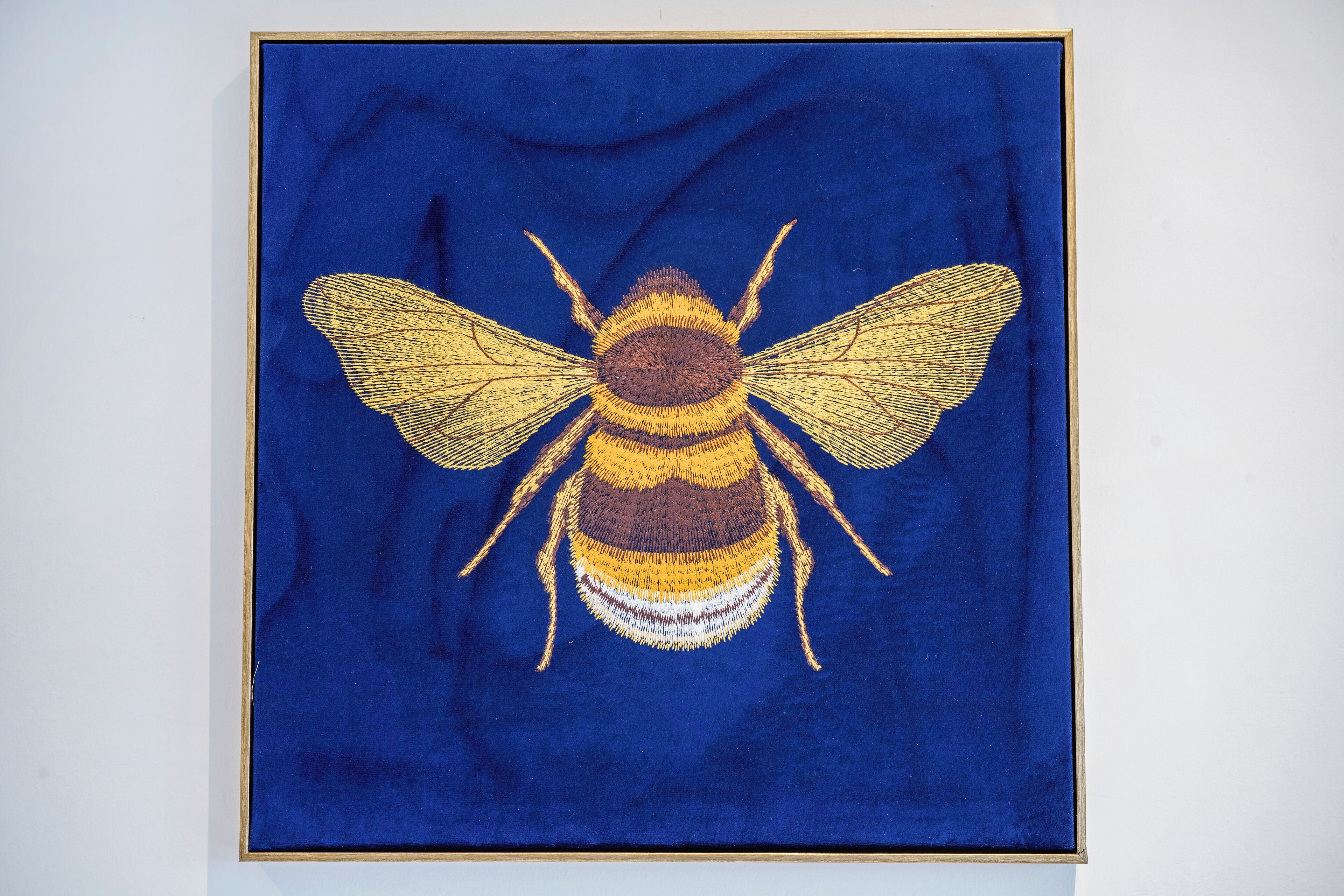 A framed artwork of a bee on a blue background.