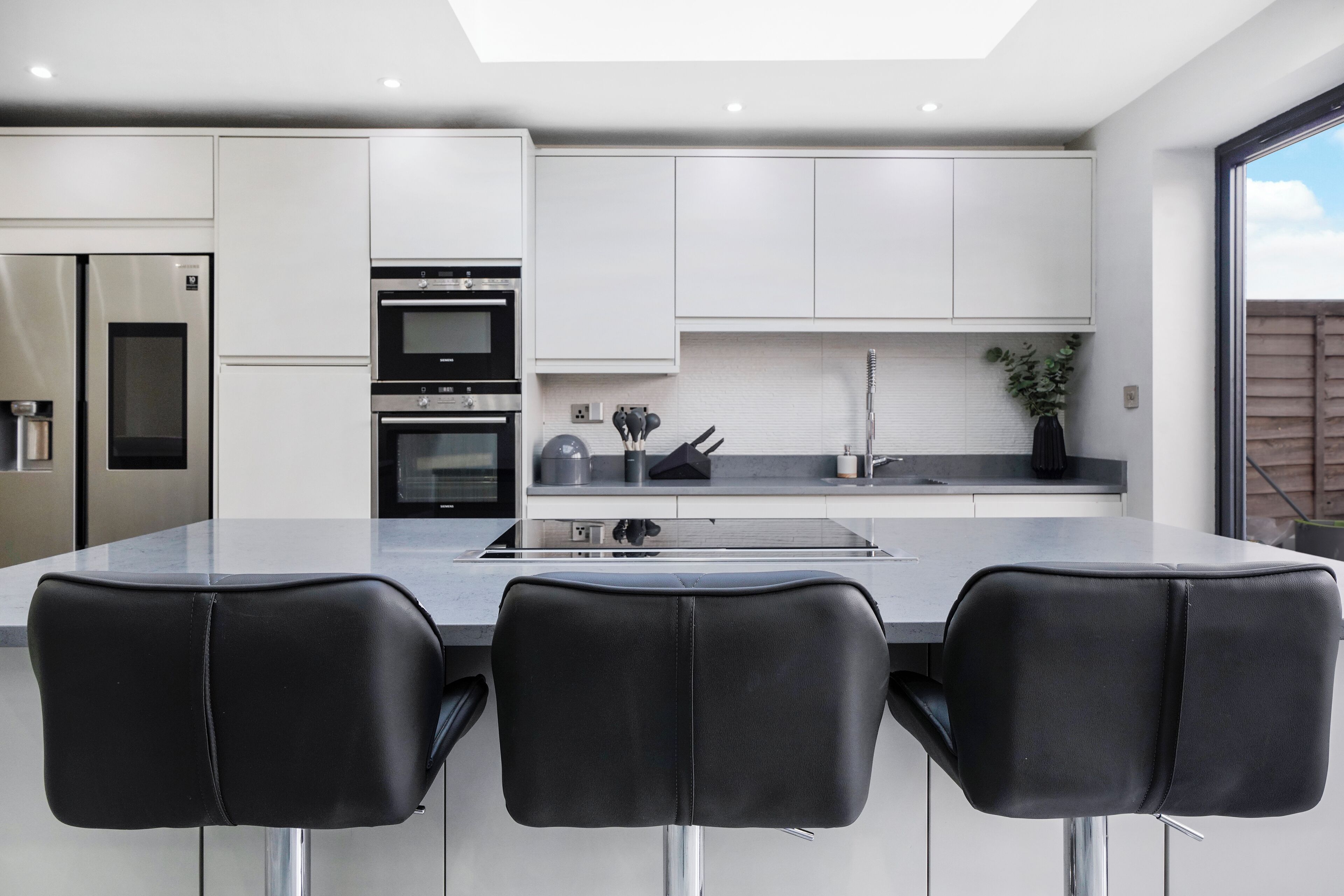Una cocina moderna con gabinetes blancos, electrodomésticos de acero inoxidable y una isla grande con taburetes negros.