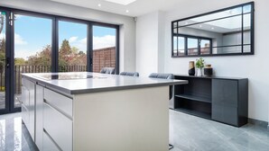 A modern kitchen with a central island, large windows, and a built-in bench. - Mount Park Rd Flat (Pinner)