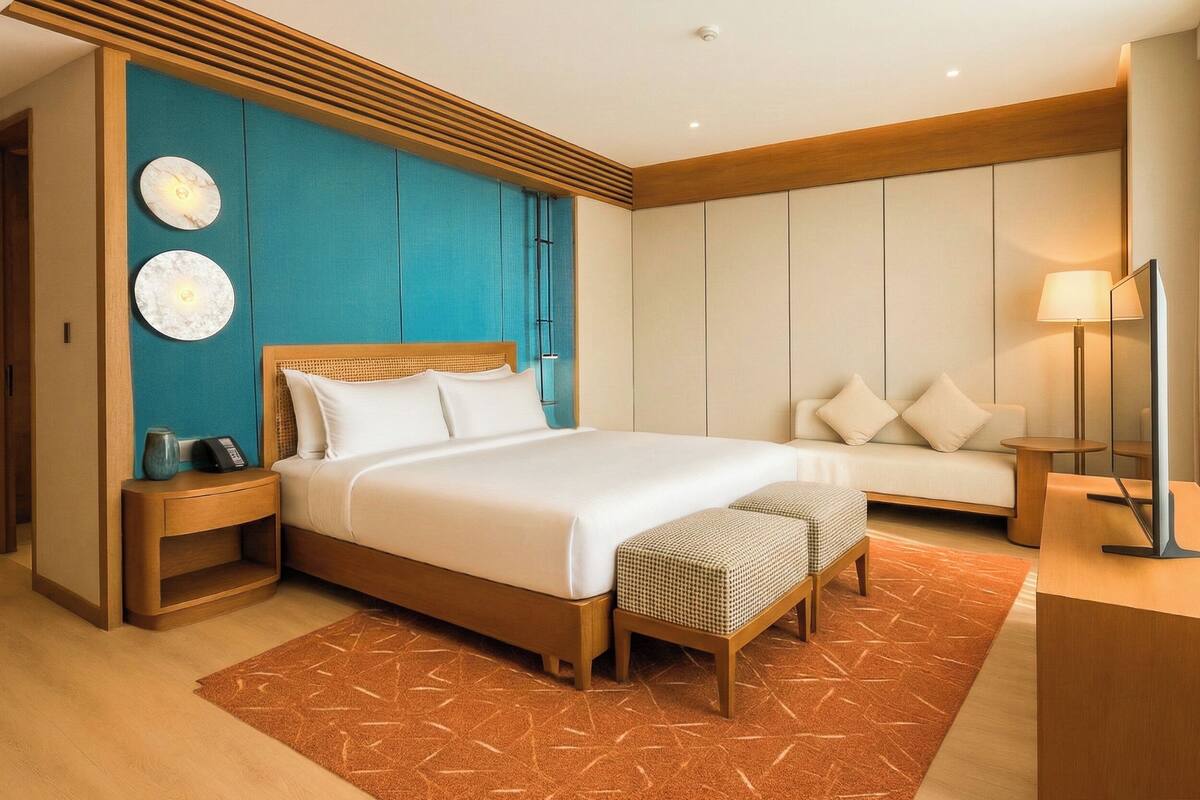 Une chambre d’hôtel moderne avec un grand lit, un canapé, une petite table et une lampe de chevet.