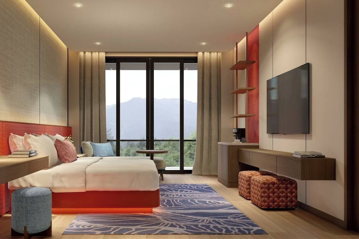 Une chambre d’hôtel moderne avec un grand lit, une télévision, un balcon offrant une vue sur les montagnes et un mur d’accent rouge.