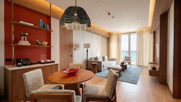 Habitación de hotel con comedor, sofá, sillón, lámpara y vista al mar.