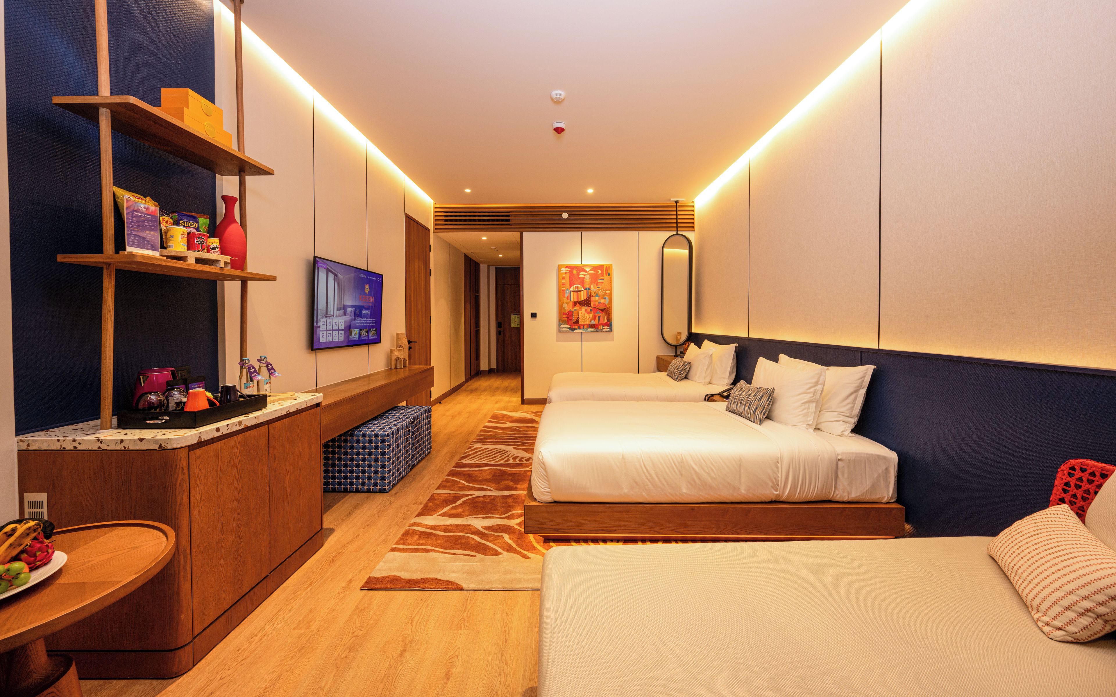Habitación de hotel con un escritorio de madera, televisor, cama con ropa blanca y un cuadro grande en la pared.
