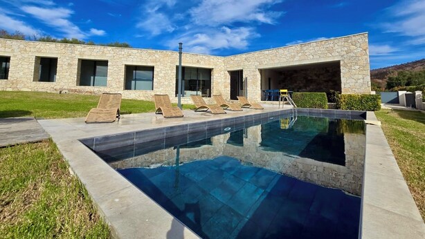 Una casa moderna con piscina, fachada de piedra y zona de estar al aire libre.