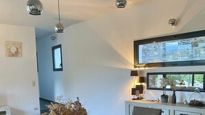 Un comedor moderno con una mesa y sillas de madera, un jarrón con flores secas, luces colgantes y vistas a través de un amplio ventanal.
