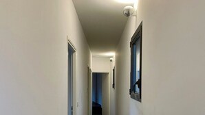 Un pasillo estrecho y bien iluminado, con paredes blancas y suelo oscuro, que conduce a una puerta al final.