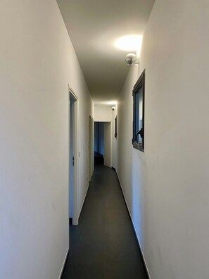 A narrow, well-lit hallway with white walls and a dark floor, leading to a door at the end. - Villa Spinelli - 4 bedrooms / private pool (oletta)