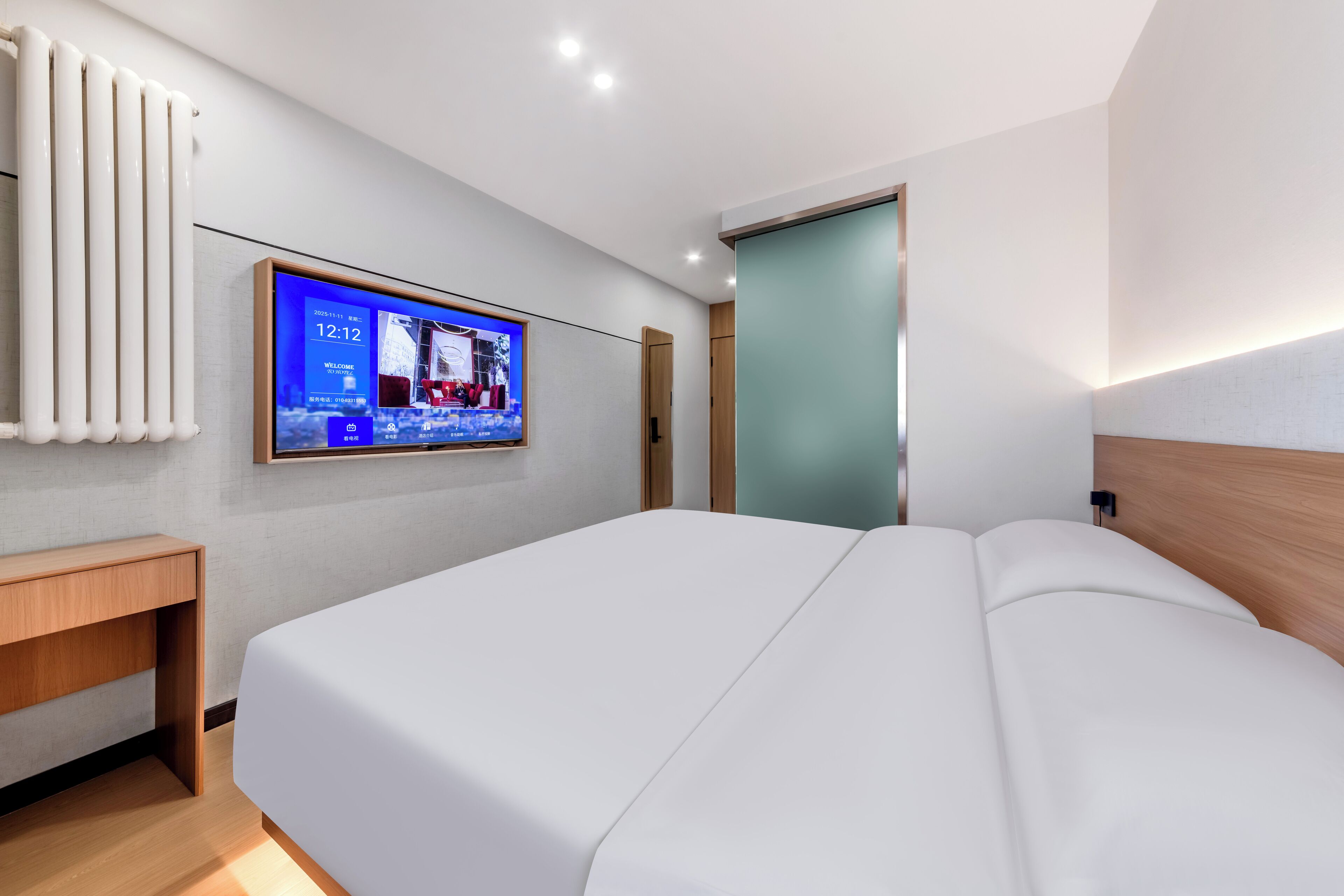 A modern hotel room with a large bed, a TV mounted on the wall, a wooden nightstand, and a radiator.