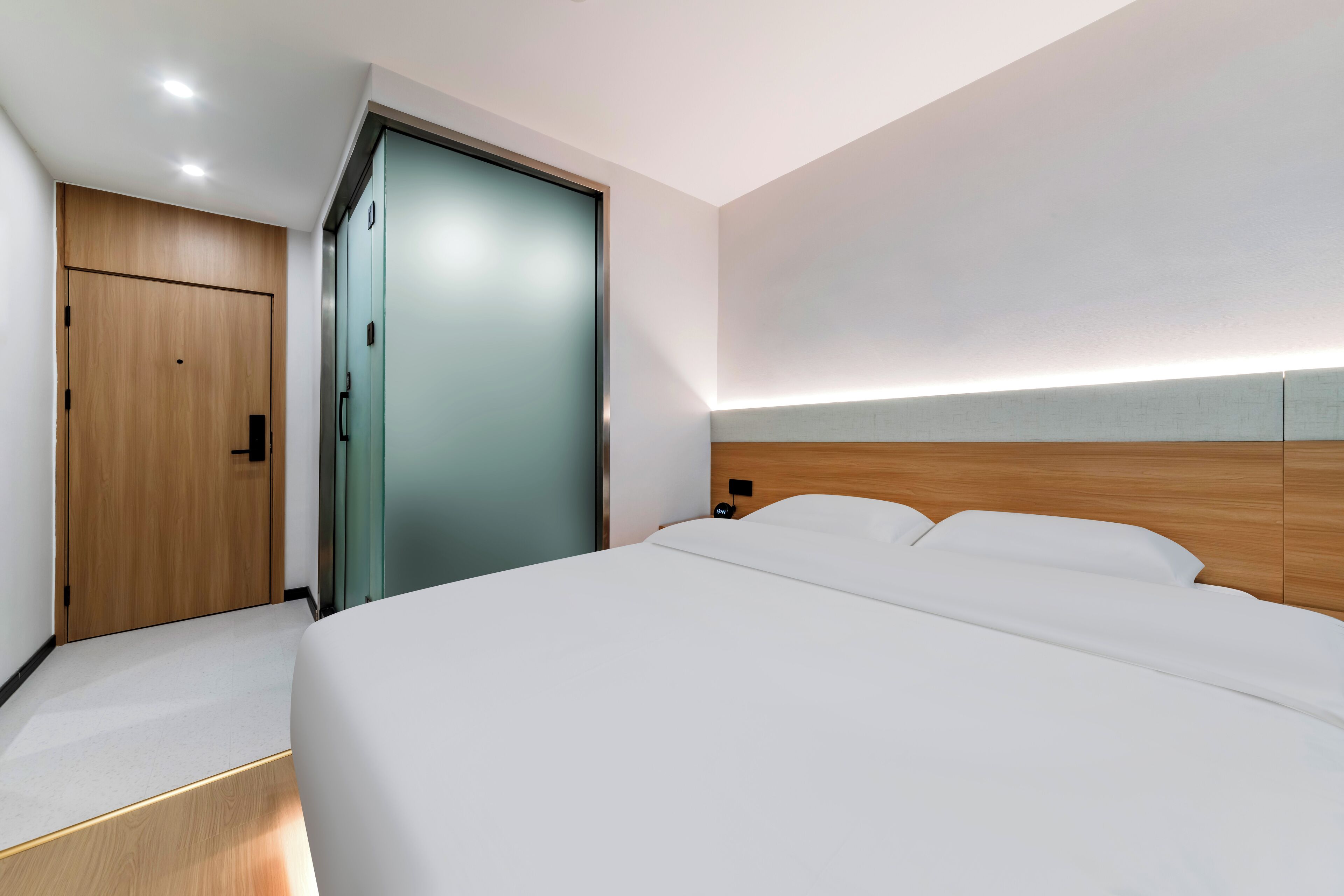 A modern hotel room with a large bed, a wooden wardrobe, and a glass door.